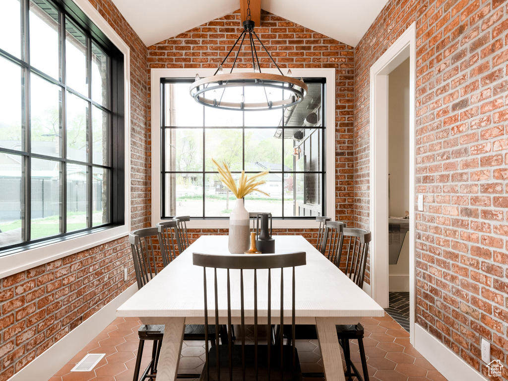 Tiled dining space featuring lofted ceiling with beams, brick wall, and a chandelier
