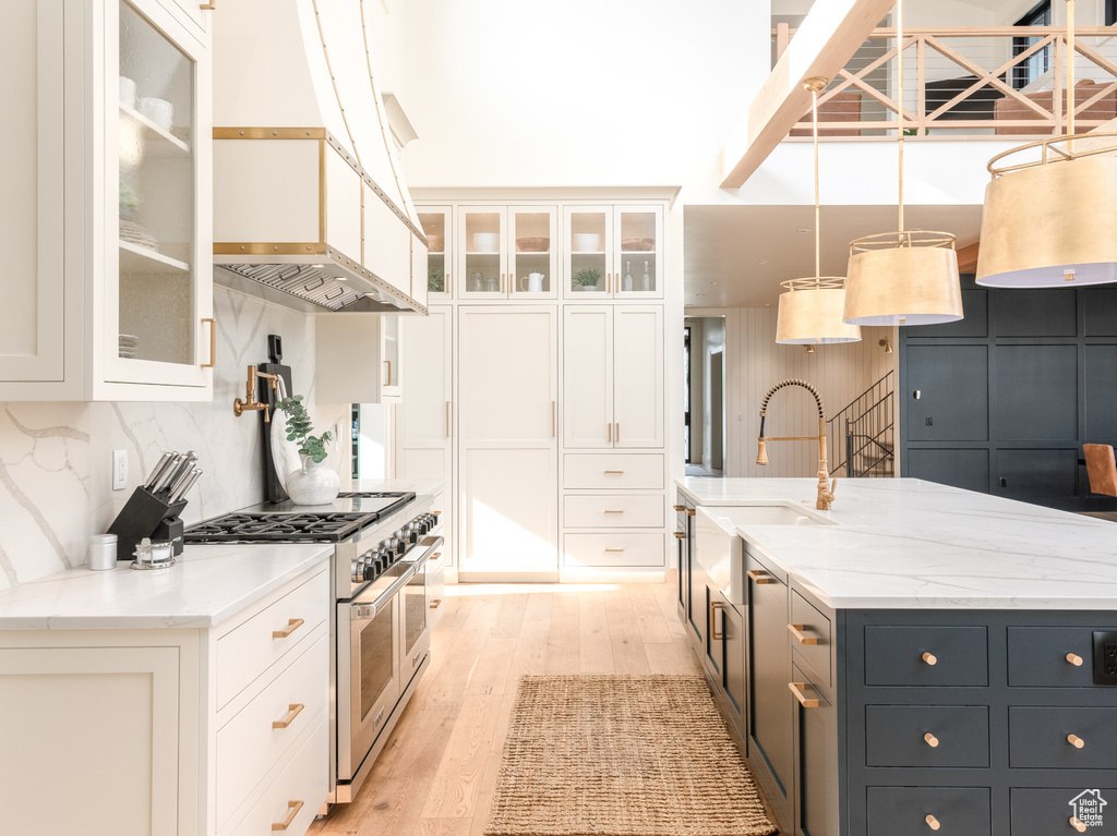 Kitchen with range with two ovens, white cabinetry, and custom range hood