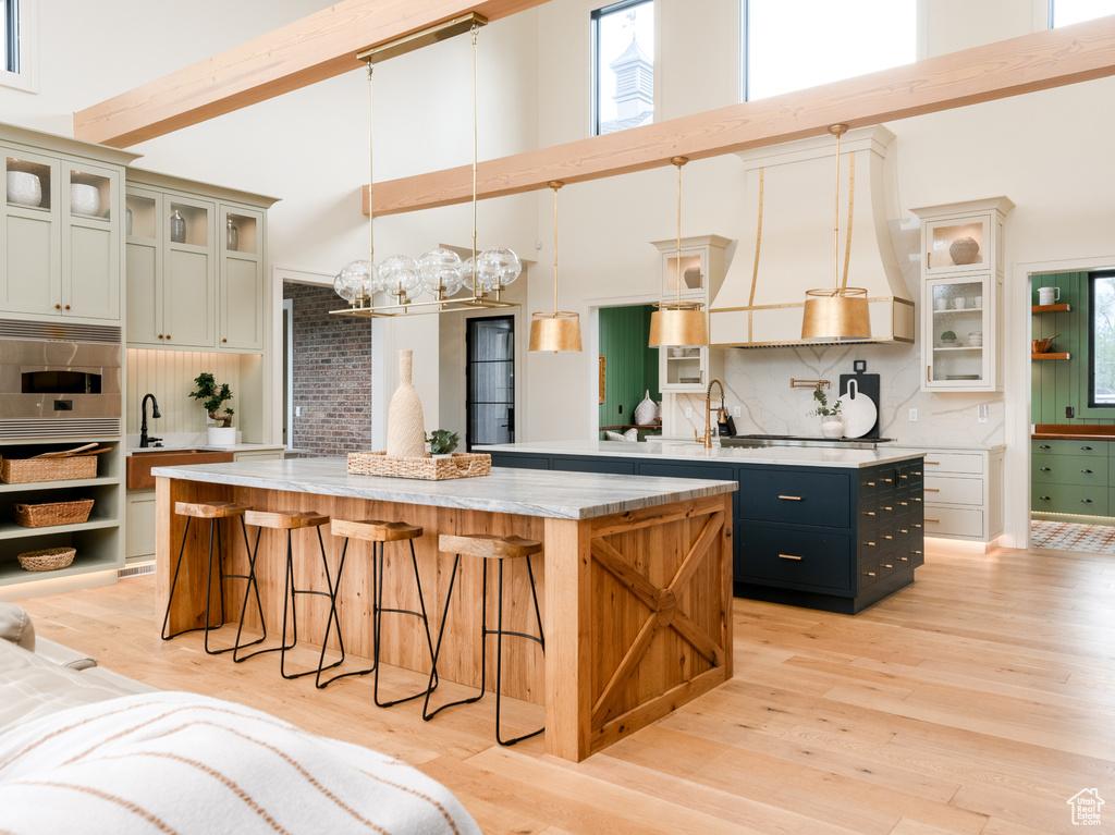 Kitchen featuring a center island with sink, backsplash, a towering ceiling, and pendant lighting