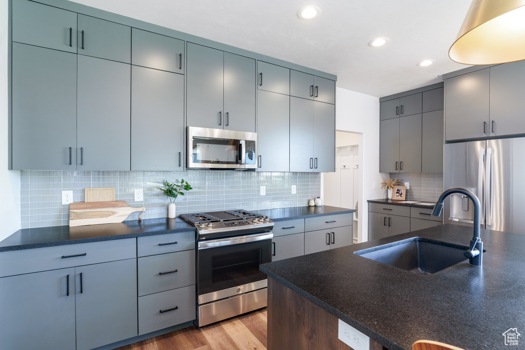 Kitchen with tasteful backsplash, appliances with stainless steel finishes, sink, and light wood-type flooring
