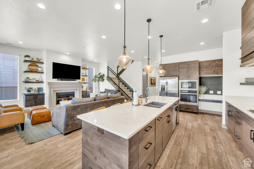 Kitchen featuring appliances with stainless steel finishes, hanging light fixtures, a center island with sink, light hardwood / wood-style floors, and sink