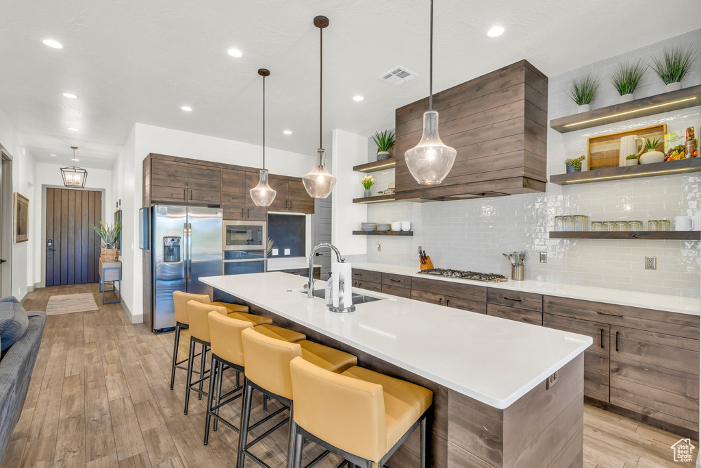 Kitchen featuring backsplash, light hardwood / wood-style flooring, stainless steel appliances, a kitchen island with sink, and sink