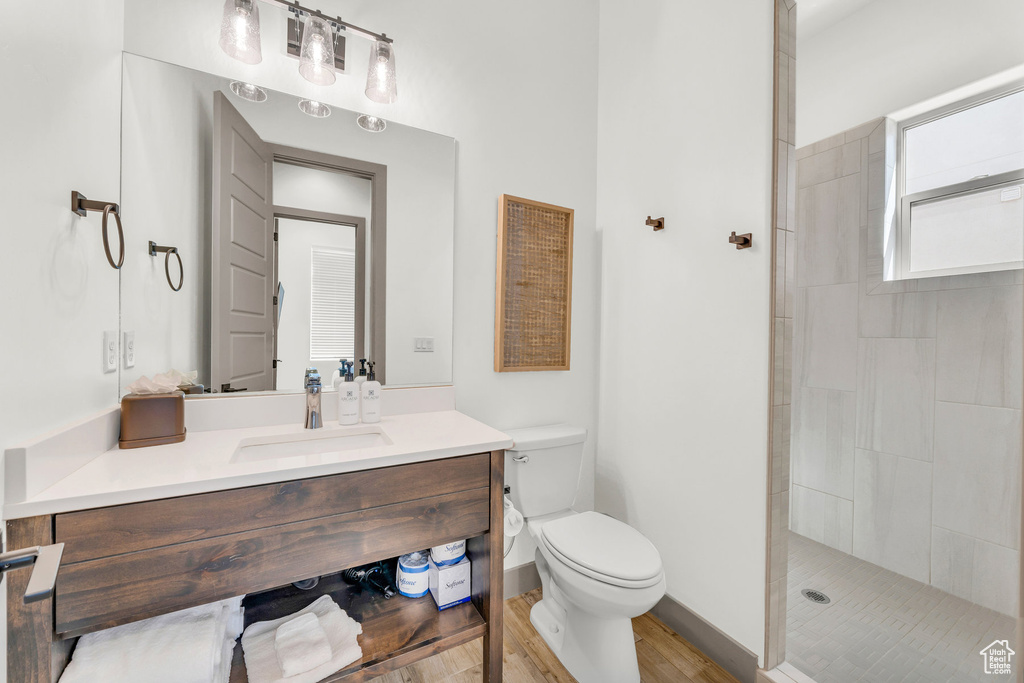 Bathroom featuring oversized vanity, hardwood / wood-style floors, tiled shower, and toilet