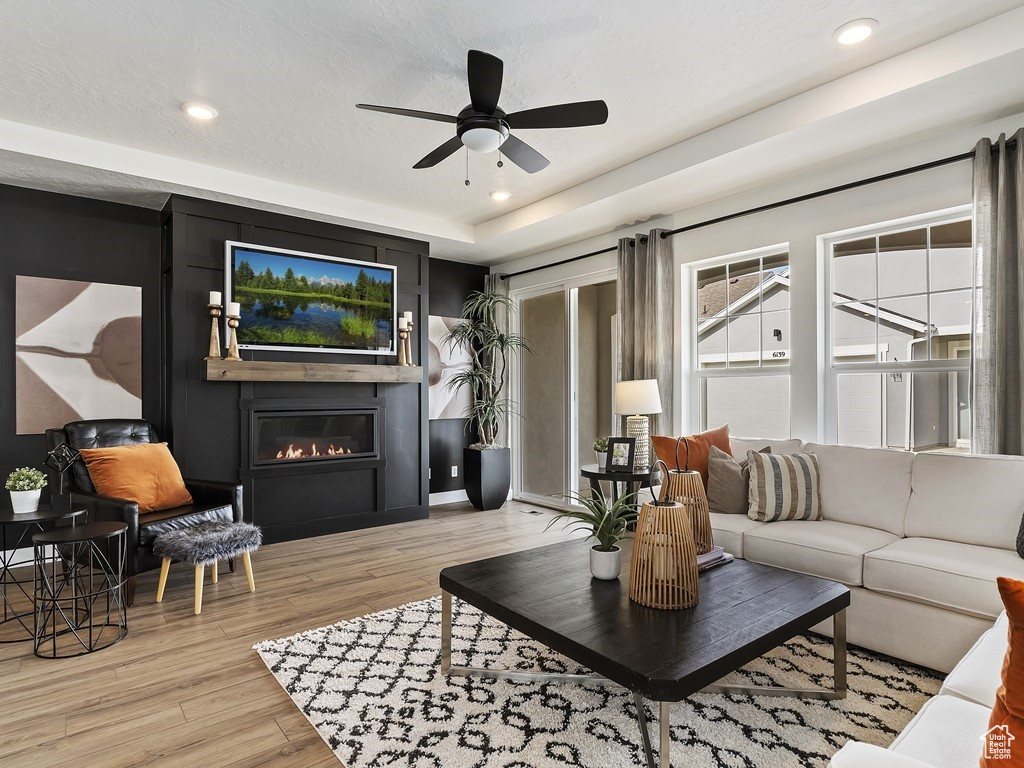 Living room featuring light hardwood / wood-style flooring, ceiling fan, and a tray ceiling