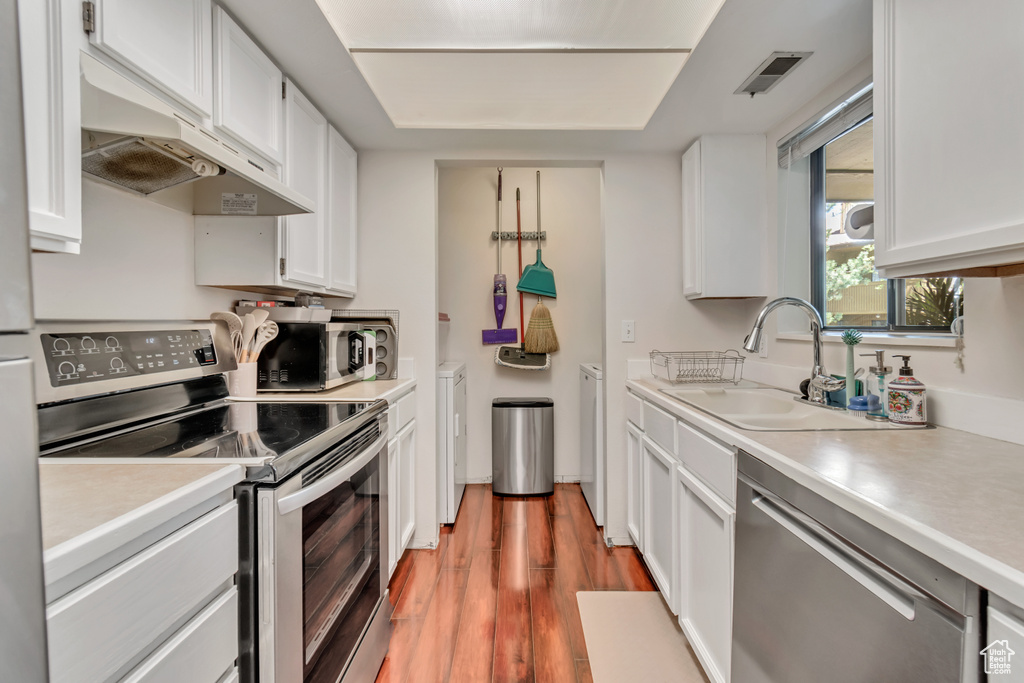 Kitchen featuring custom exhaust hood, white cabinets, sink, hardwood / wood-style floors, and stainless steel appliances
