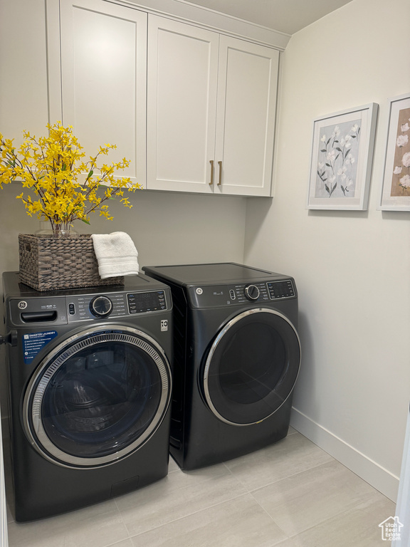 Clothes washing area with independent washer and dryer, cabinets, and light tile floors