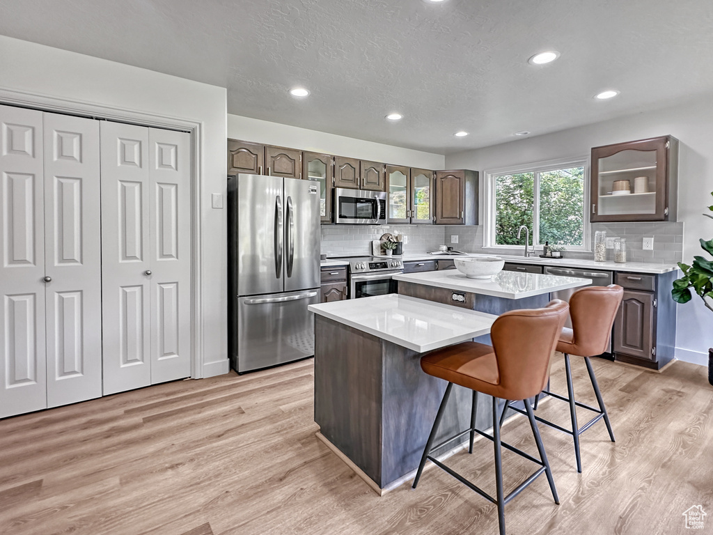 Kitchen featuring a kitchen island, tasteful backsplash, stainless steel appliances, and light wood-type flooring