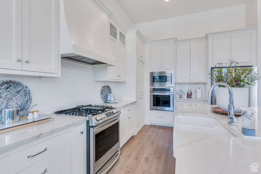 Kitchen featuring premium range hood, stainless steel appliances, light hardwood / wood-style floors, tasteful backsplash, and light stone counters