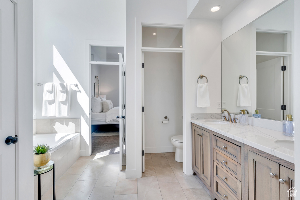 Bathroom with oversized vanity, toilet, tile flooring, tiled bath, and dual sinks