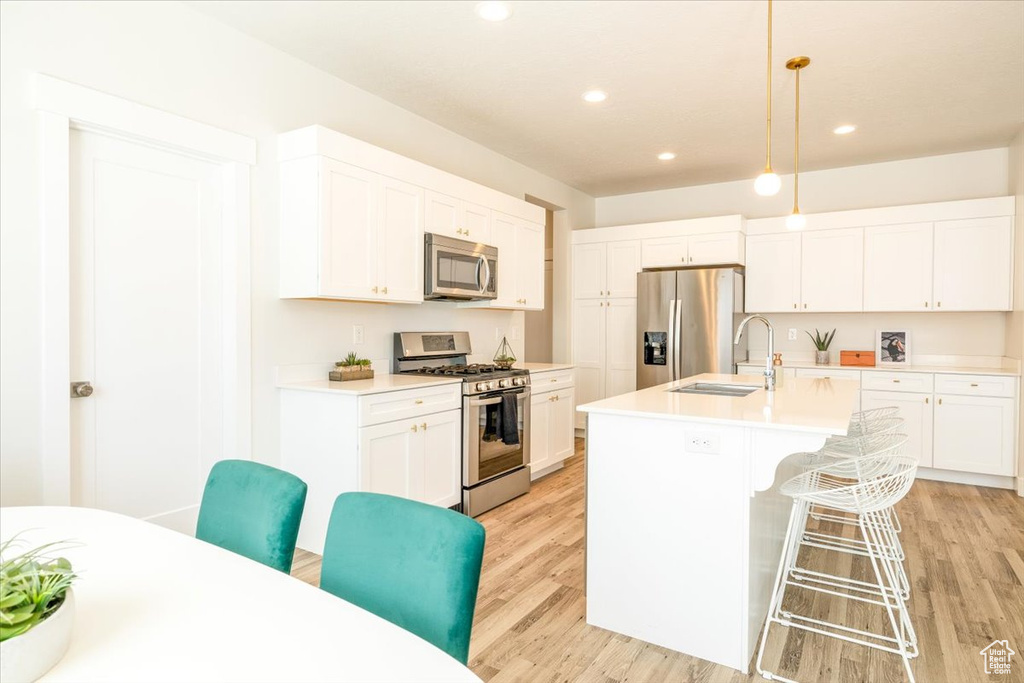 Kitchen featuring white cabinets, a center island with sink, light hardwood / wood-style flooring, and stainless steel appliances