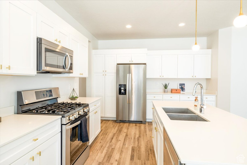 Kitchen with sink, light wood-type flooring, white cabinetry, hanging light fixtures, and stainless steel appliances