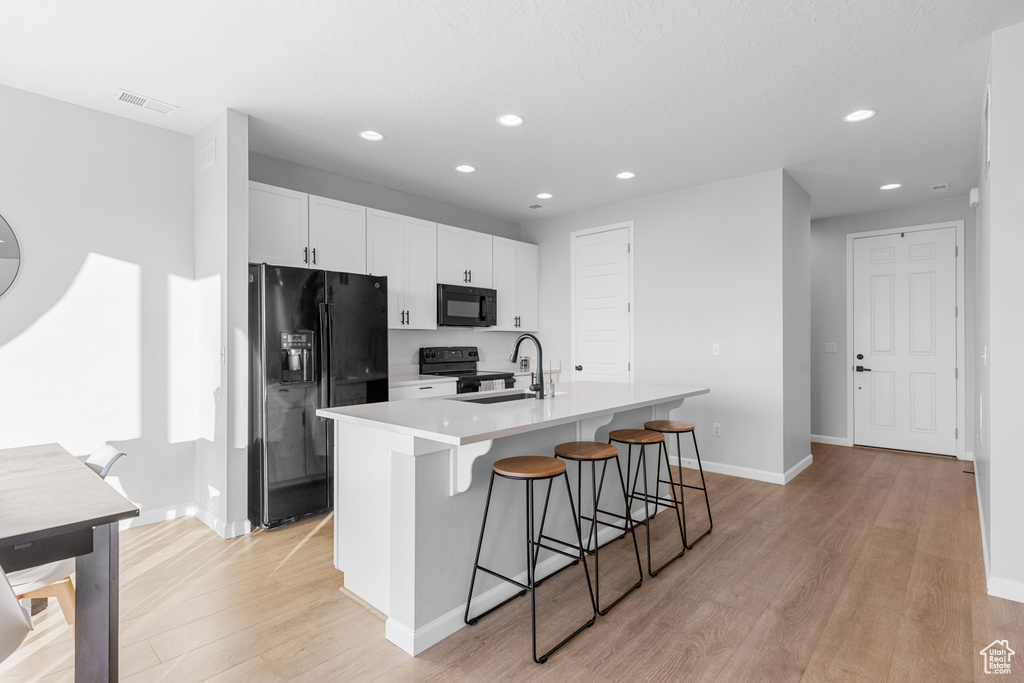 Kitchen featuring white cabinets, sink, black appliances, light hardwood / wood-style flooring, and a kitchen island with sink