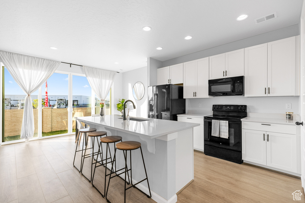 Kitchen featuring plenty of natural light, sink, a center island with sink, and black appliances