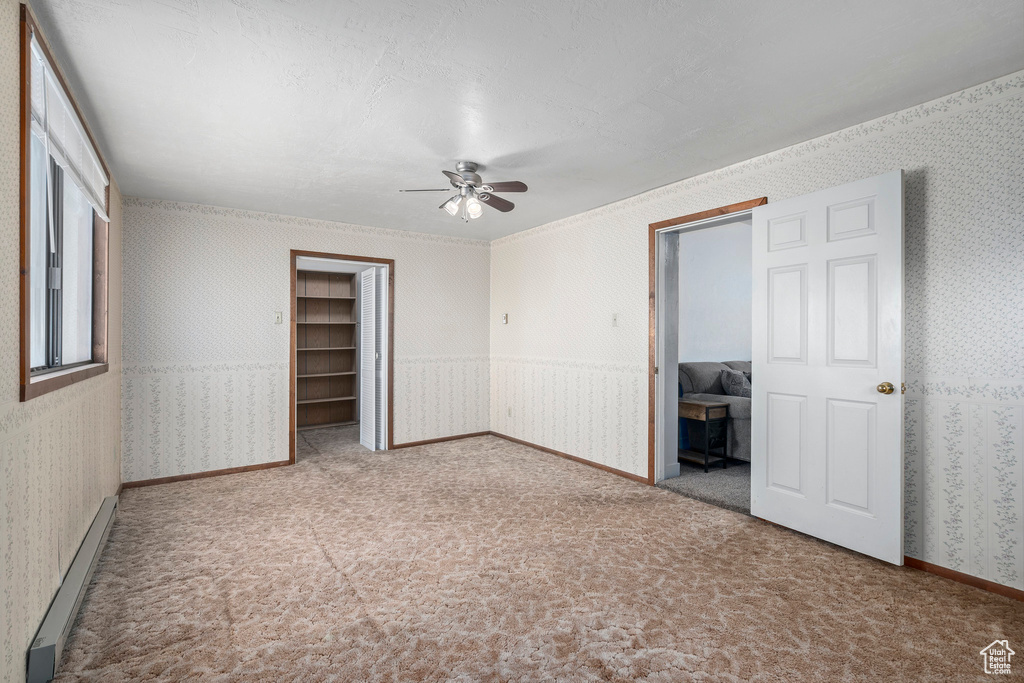 Unfurnished bedroom featuring carpet, a closet, a baseboard heating unit, ceiling fan, and a walk in closet