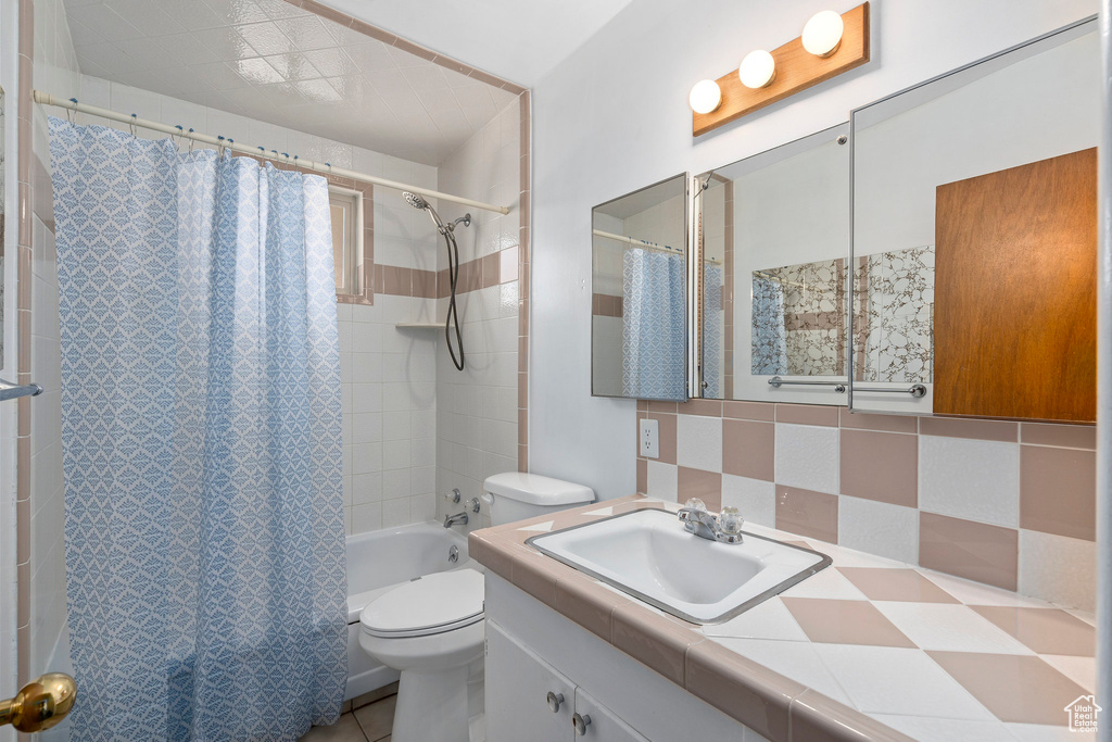 Full bathroom featuring shower / bath combo with shower curtain, tile floors, tile walls, large vanity, and toilet