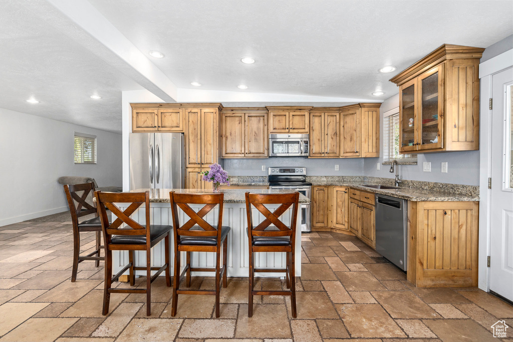 Kitchen with appliances with stainless steel finishes, a kitchen island, tile flooring, light stone counters, and sink
