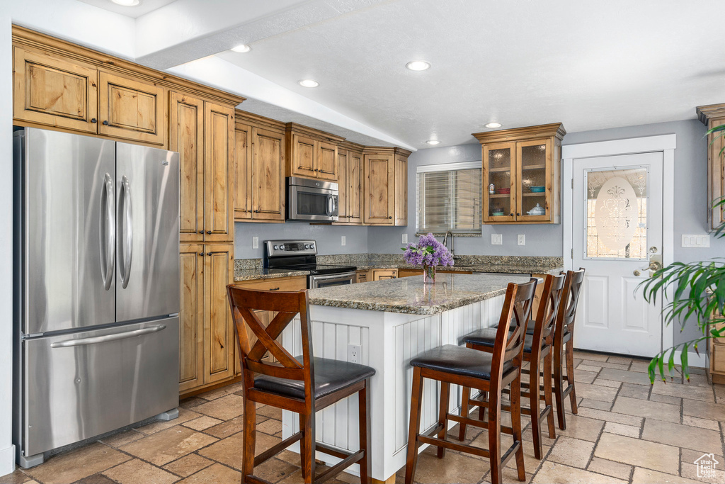 Kitchen with a center island, appliances with stainless steel finishes, light tile floors, and light stone counters