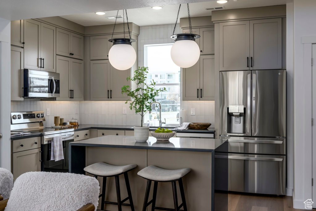 Kitchen featuring appliances with stainless steel finishes, dark hardwood / wood-style floors, a kitchen island, and backsplash