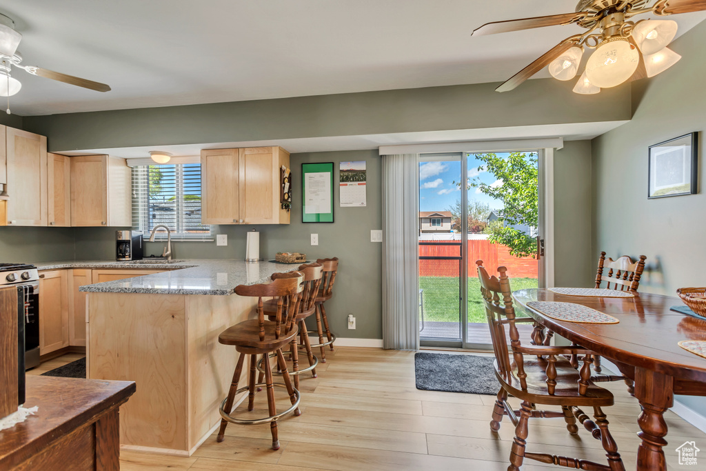 Kitchen with ceiling fan, sink, light hardwood / wood-style flooring, kitchen peninsula, and a kitchen breakfast bar
