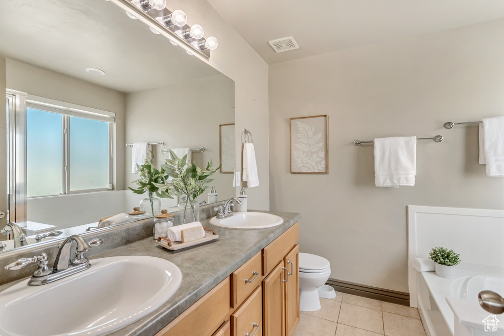 Bathroom featuring large vanity, dual sinks, toilet, tile floors, and a bath to relax in