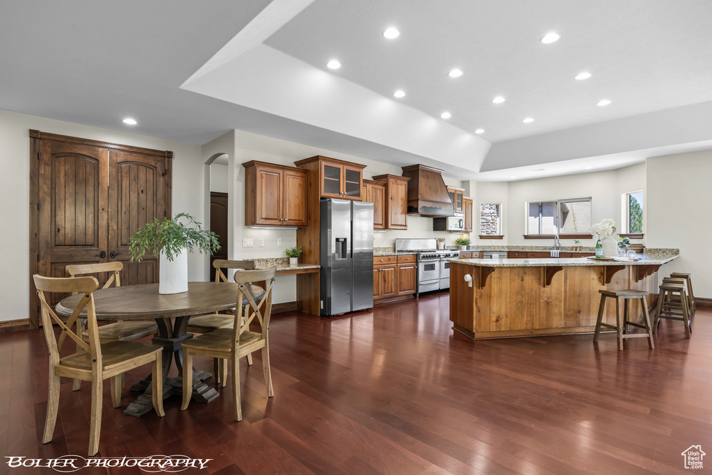 Kitchen with light stone counters, a tray ceiling, stainless steel appliances, dark hardwood / wood-style floors, and premium range hood