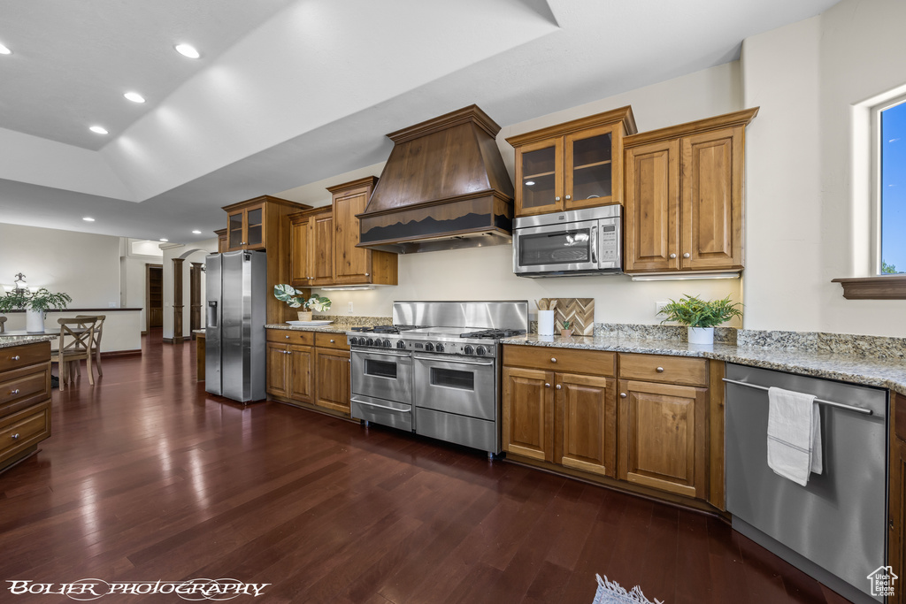 Kitchen with custom range hood, dark hardwood / wood-style floors, appliances with stainless steel finishes, and light stone counters