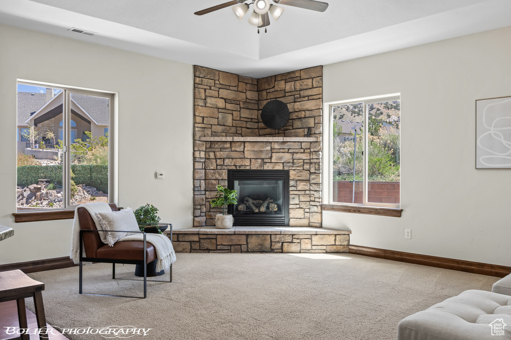 Carpeted living room featuring plenty of natural light, a stone fireplace, and ceiling fan