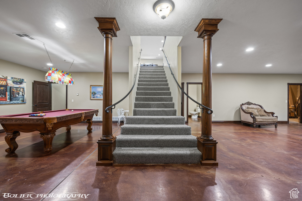 Staircase with a textured ceiling, pool table, concrete floors, and decorative columns
