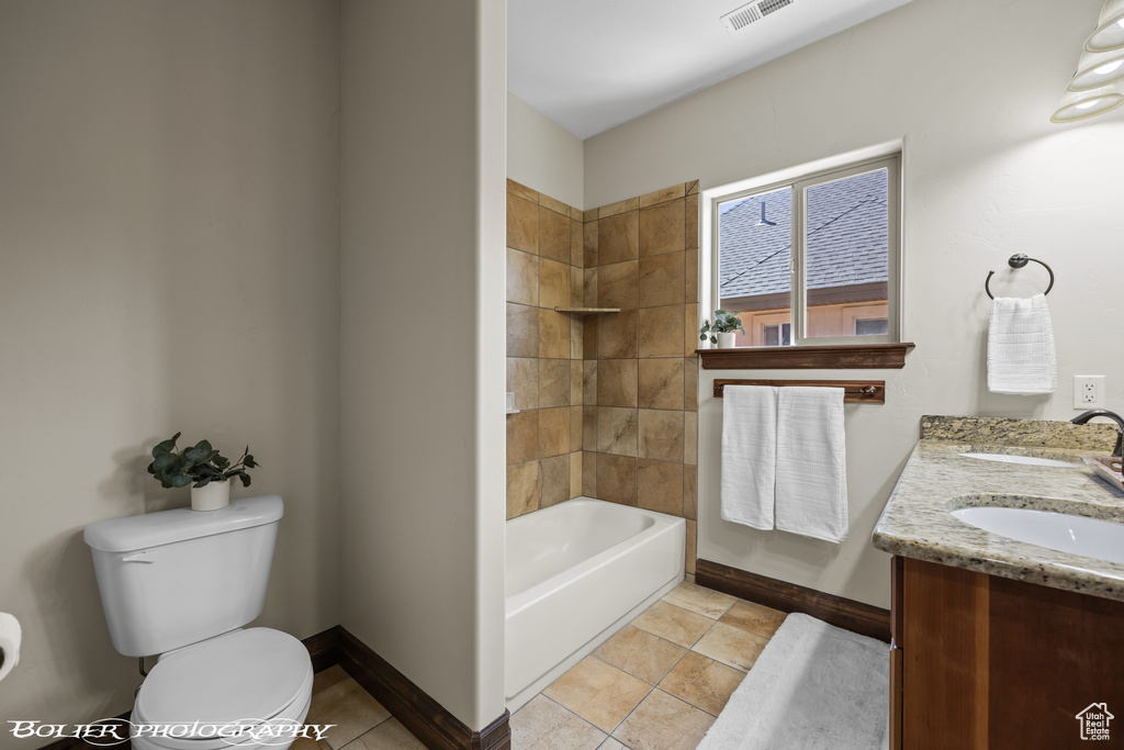 Full bathroom featuring tile flooring, dual vanity, tiled shower / bath, and toilet