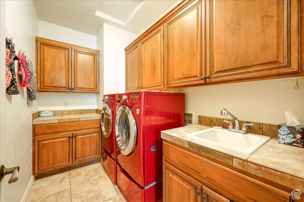 Laundry area featuring light tile floors, washing machine and dryer, cabinets, and sink