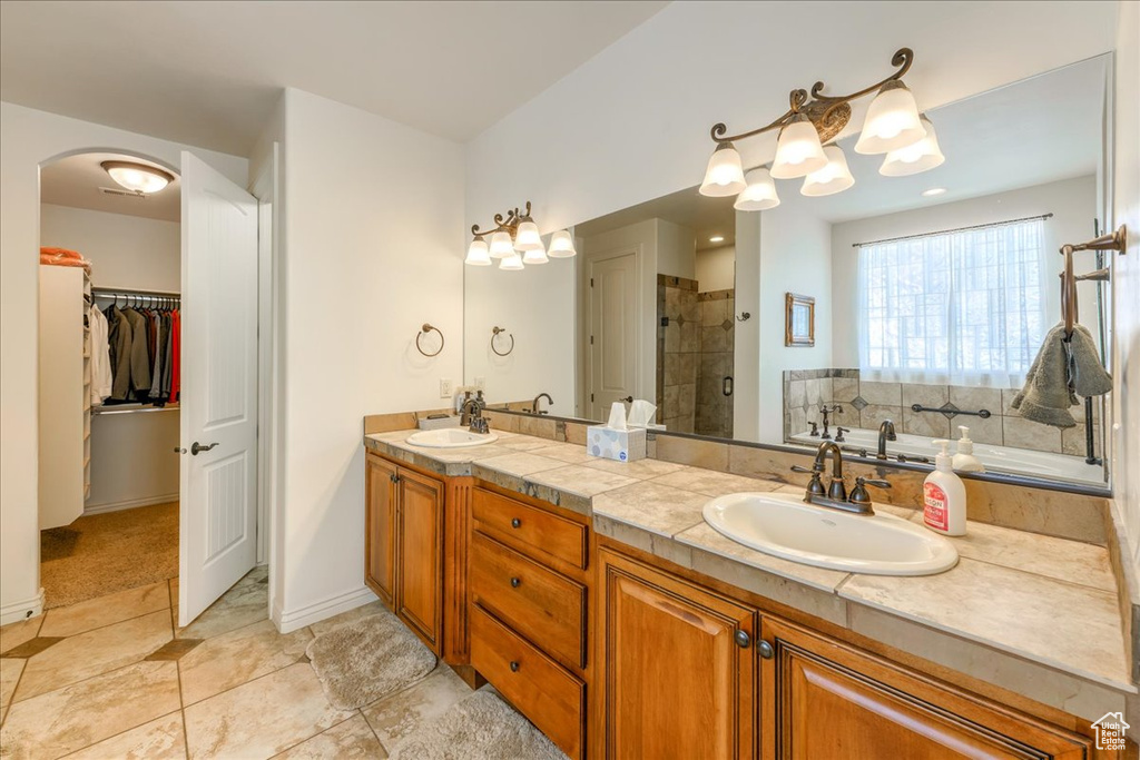 Bathroom featuring tile flooring, dual sinks, vanity with extensive cabinet space, and a tile shower