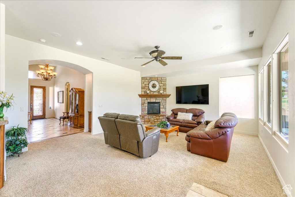 Carpeted living room with ceiling fan with notable chandelier and a stone fireplace