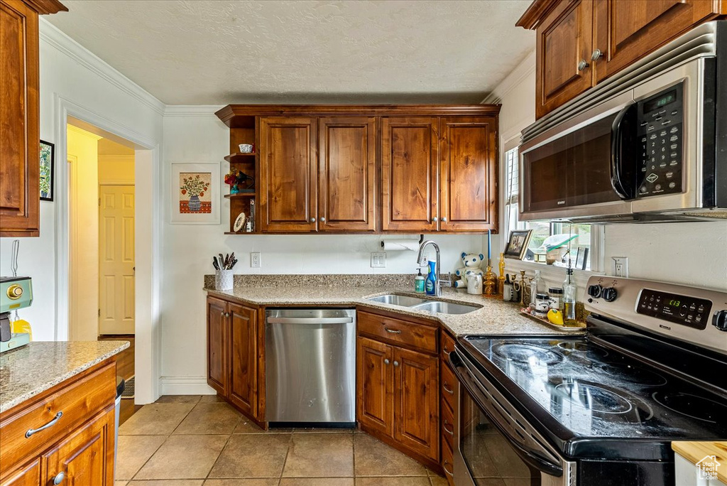 Kitchen with stainless steel appliances, light tile flooring, light stone counters, sink, and ornamental molding