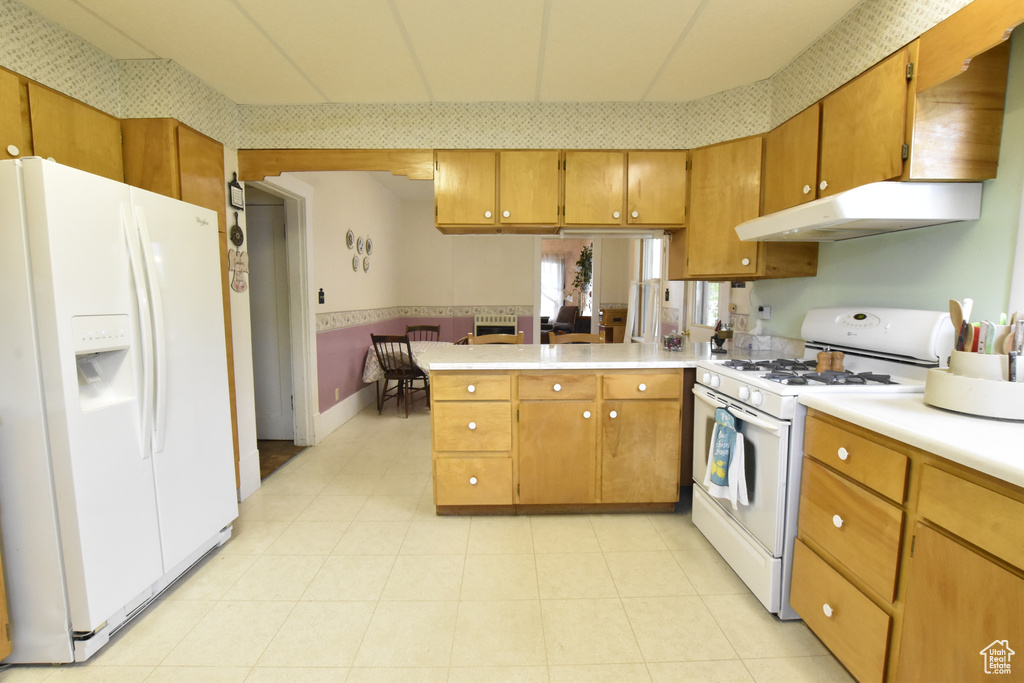 Kitchen with white appliances, kitchen peninsula, and light tile floors