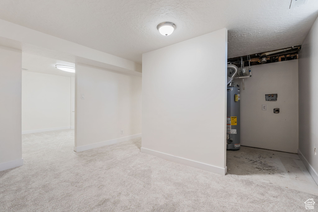 Basement featuring a textured ceiling, water heater, and light carpet