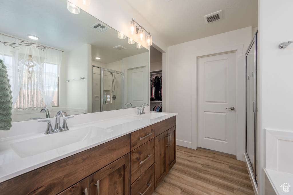 Bathroom with hardwood / wood-style floors, large vanity, a shower with shower door, and double sink