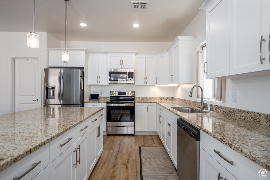 Kitchen featuring appliances with stainless steel finishes, white cabinets, sink, light hardwood / wood-style floors, and decorative light fixtures