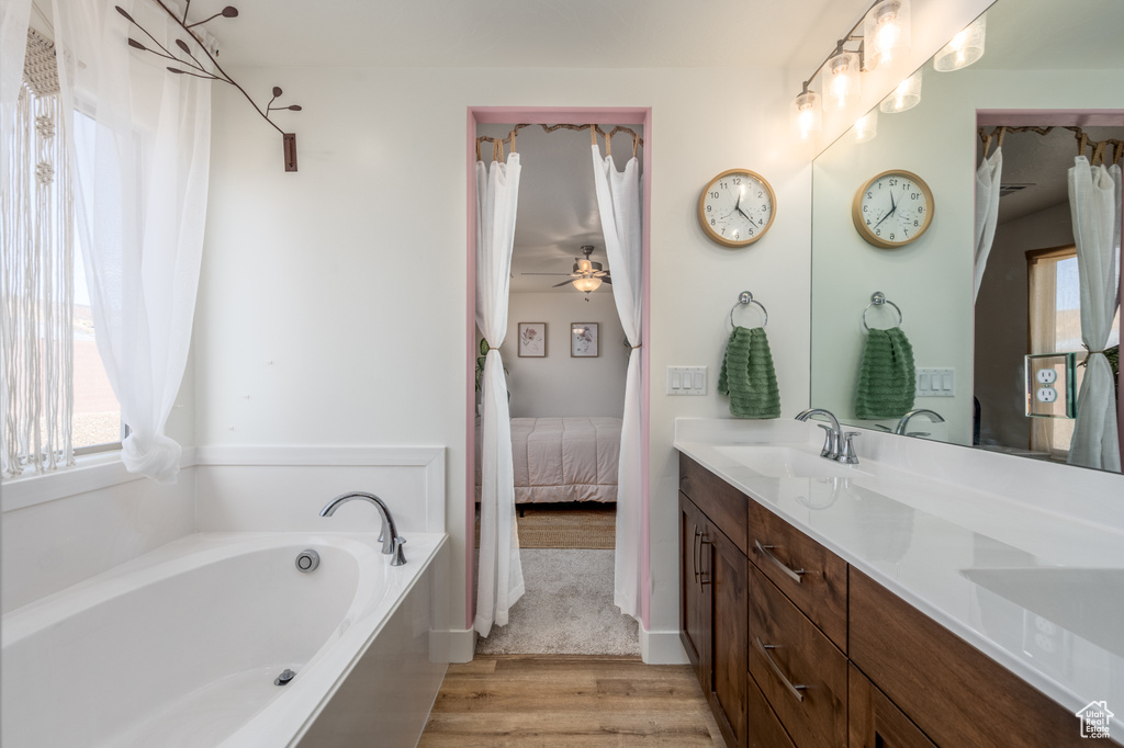 Bathroom with wood-type flooring, ceiling fan, a bath, and dual vanity