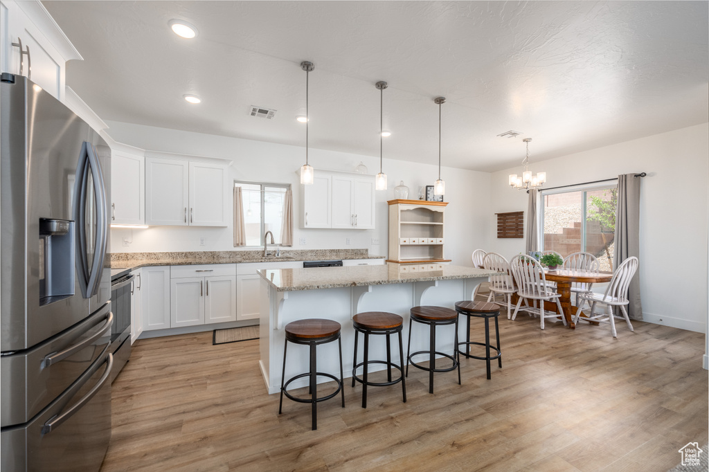 Kitchen with a center island, white cabinets, light hardwood / wood-style floors, stainless steel fridge with ice dispenser, and pendant lighting