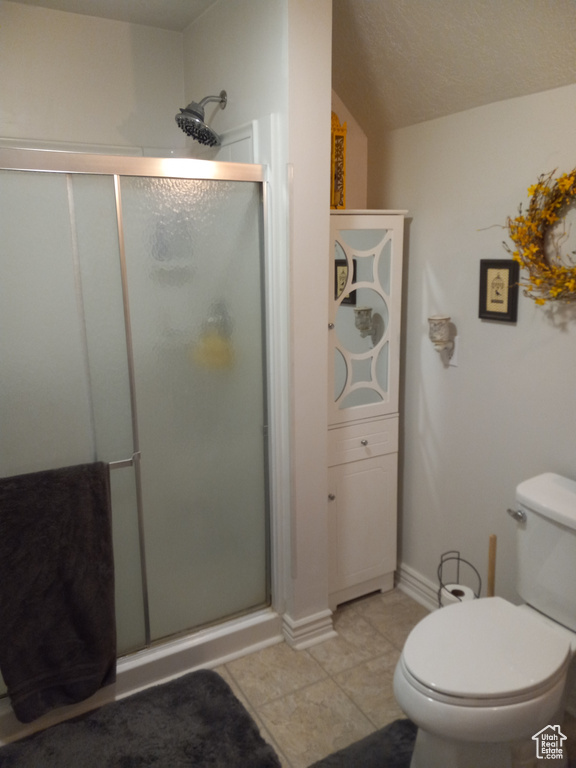 Bathroom with a shower with door, toilet, and tile flooring