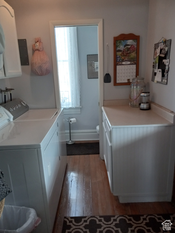 Clothes washing area with wood-type flooring, cabinets, washer and dryer, and a healthy amount of sunlight