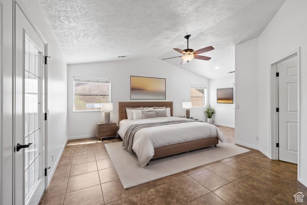 Tiled bedroom featuring lofted ceiling, ceiling fan, and a textured ceiling