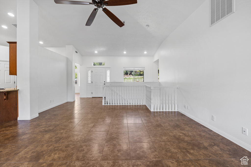 Unfurnished living room featuring vaulted ceiling, ceiling fan, and dark tile floors
