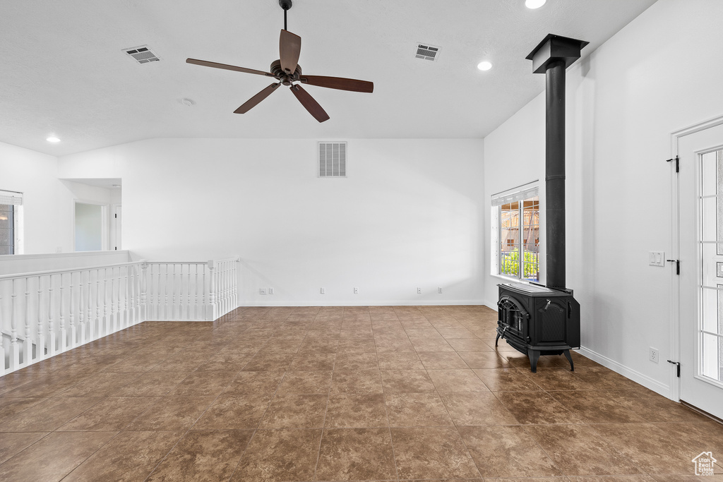 Interior space with a wood stove, tile flooring, ceiling fan, and lofted ceiling