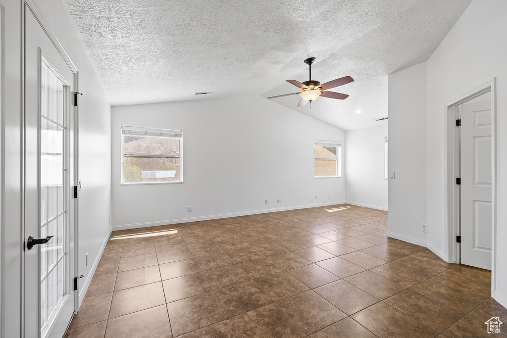 Empty room featuring a healthy amount of sunlight, dark tile floors, and vaulted ceiling