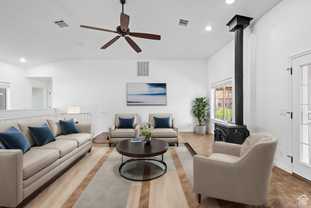 Living room featuring vaulted ceiling, a wood stove, ceiling fan, and light hardwood / wood-style floors