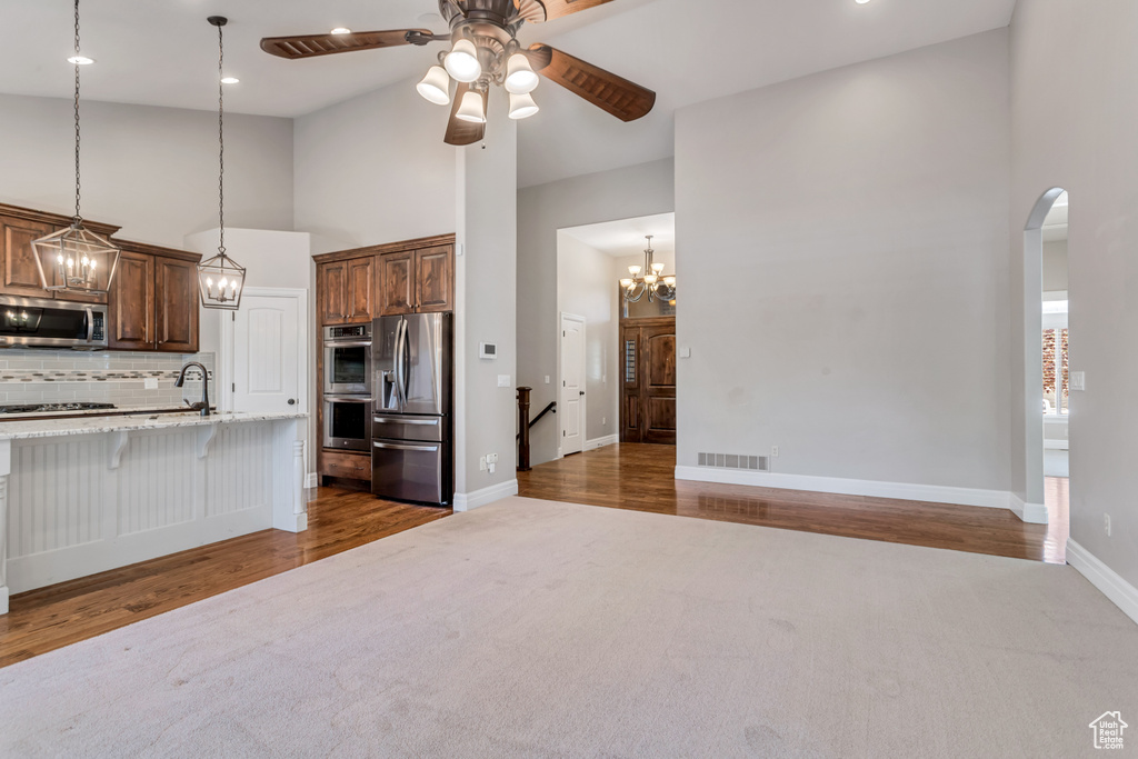 Kitchen with pendant lighting, high vaulted ceiling, appliances with stainless steel finishes, ceiling fan with notable chandelier, and dark carpet
