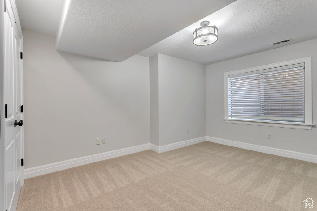 Empty room featuring light colored carpet and a textured ceiling