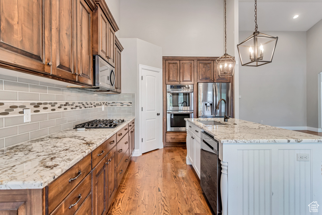 Kitchen with appliances with stainless steel finishes, light hardwood / wood-style flooring, hanging light fixtures, a center island with sink, and tasteful backsplash