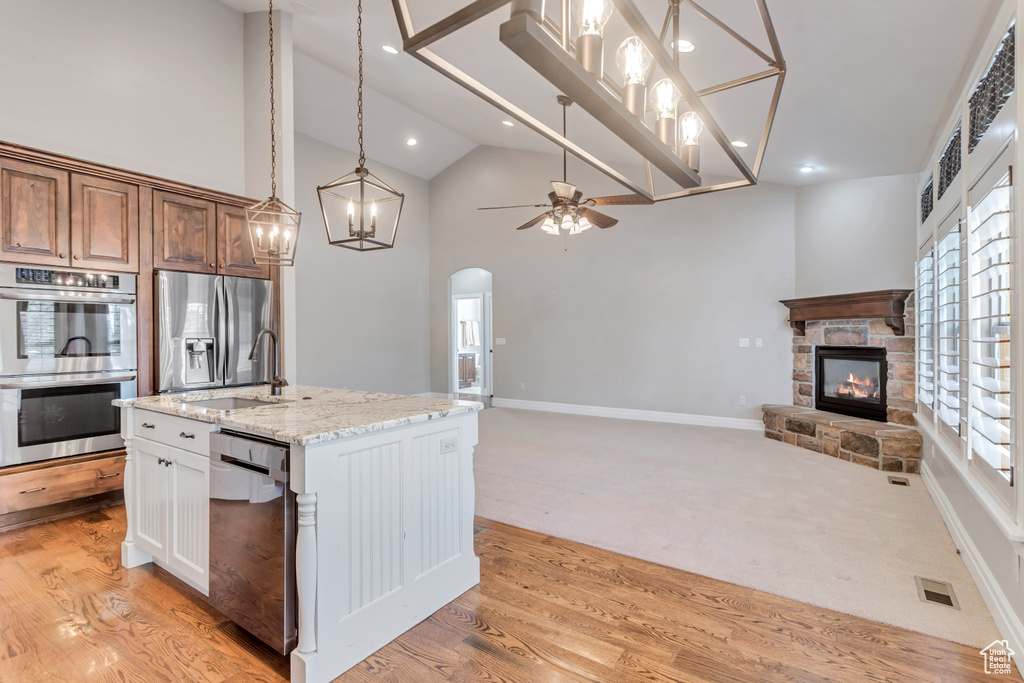 Kitchen featuring a fireplace, stainless steel appliances, light stone counters, light colored carpet, and ceiling fan